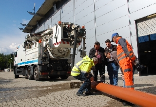 people in workwaer standing in front of sewer cleaning vehicle