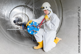 man in white overall with yellow helmet working on pressure sewer pipe test rig