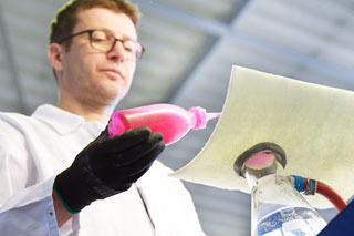 Man in white coat with bottle with pink liquid at CIPP liner sample in laboratory
