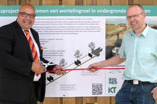 Two men in front of information board cutting red rope