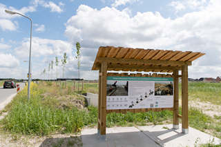 wooden stand with information board in front of test facility with row of young trees