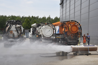 water spraying from pipe in front of three sewer cleaning vehicles